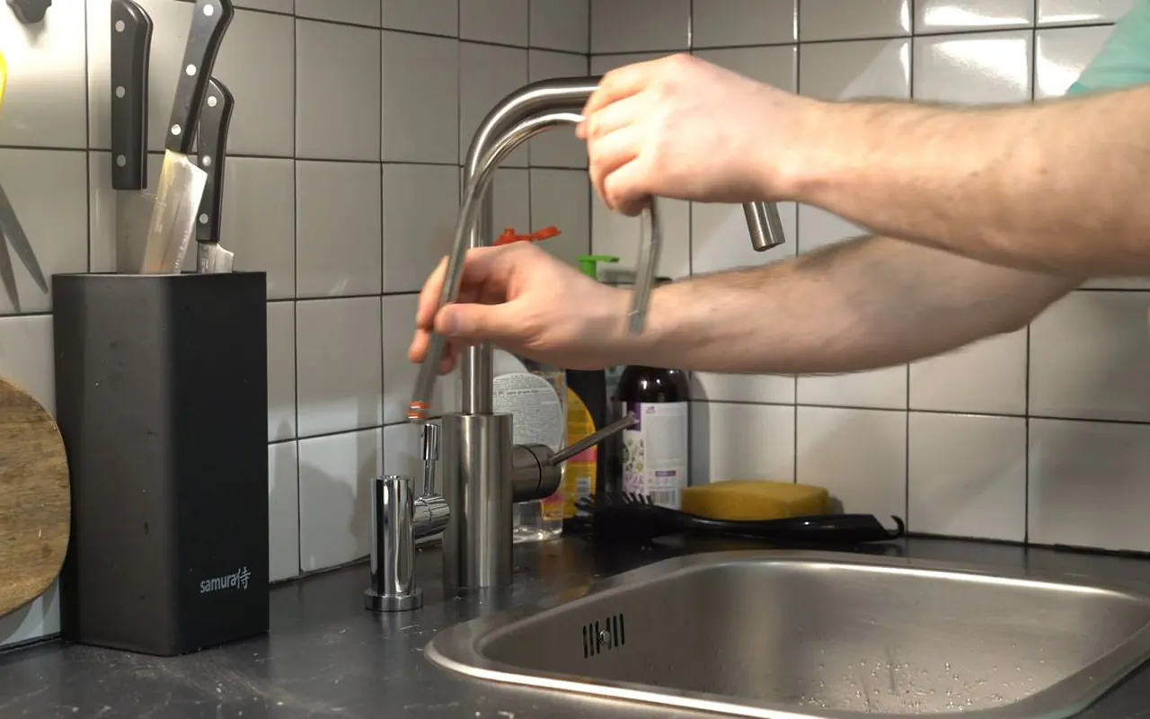 Hands adjusting a kitchen faucet above a stainless steel sink